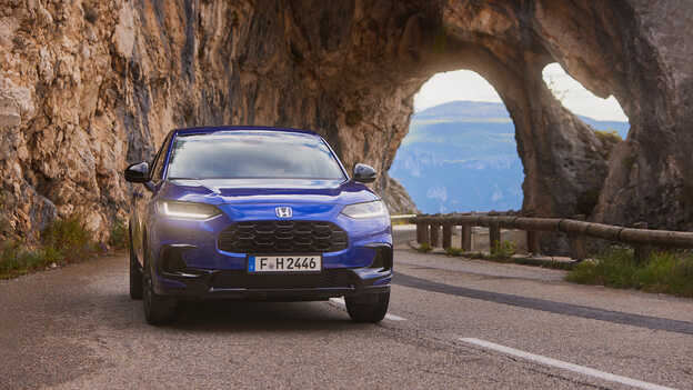 A ZR-V hibrid SUV kék színben, sportos megjelenéssel egy hegyi úton halad.