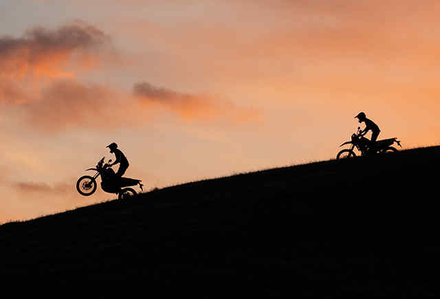 Két 300-as sorozatú Honda motorkerékpár a naplementében halad lefelé egy domboldalon
