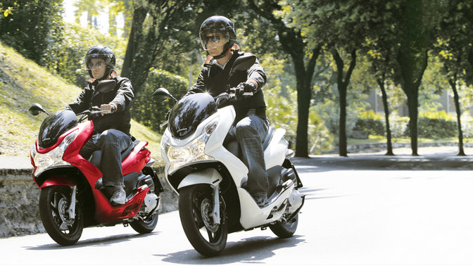 Egy fehér és egy piros PCX, vezetővel, háromnegyedes nézetben. (Helyszín).