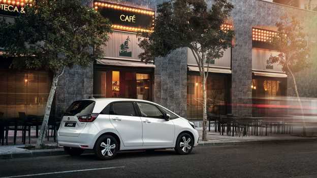 Kávézó előtt parkoló hibrid Honda Jazz hátulról.
