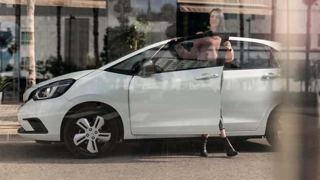 Parkoló Honda Jazz oldalnézetből, amelynek egy hölgy kinyitja az ajtaját