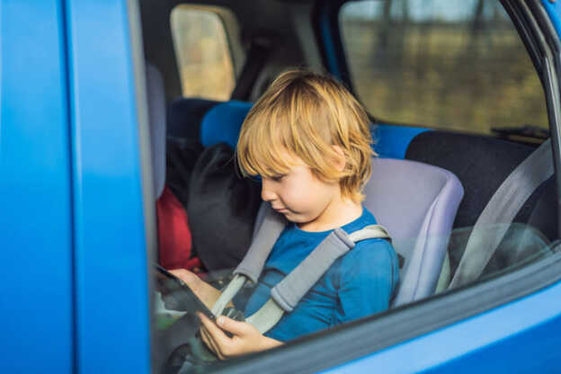 Egy autós kirándulás során táblagépen játszó fiú