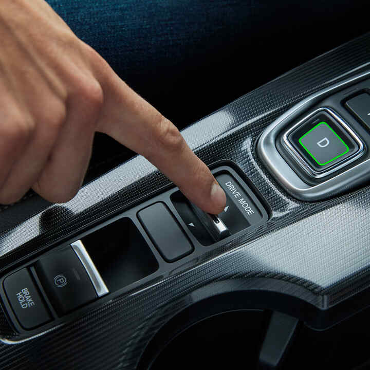 Közeli felvétel egy személyről a Civic Hybrid belsejében, amint beállítja az autó vezetési módját.