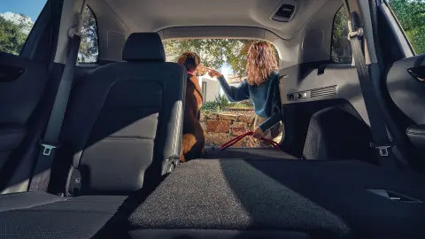 CR-V Hybrid SUV ledöntött hátsó ülés, amelyen egy nő ül, a nyitott csomagtérben pedig egy kutya látható. 