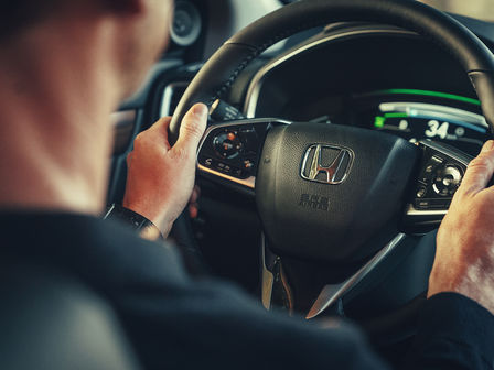 Közelkép a Honda CR-V Hybridről az autóban ülő modellel és kormánykerékkel.