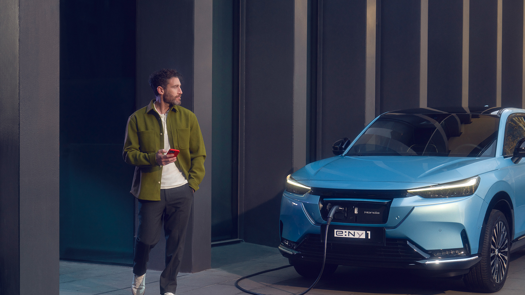 Egy férfi sétál a Honda e:Ny1 mellett, amely épp be van dugva és töltődik.