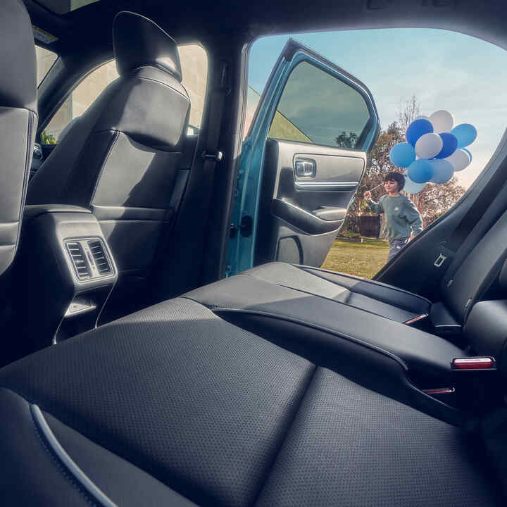 Közelkép a Honda e:Ny1 hátsó üléséről, a nyitott ajtó előtt sétáló gyermeknél léggömbök vannak.