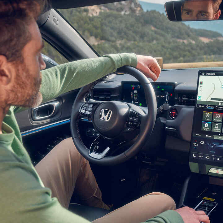 Egy férfi a Honda e:Ny1-et vezeti a digitális vezetői kijelzőn megjelenő navigációt használva.