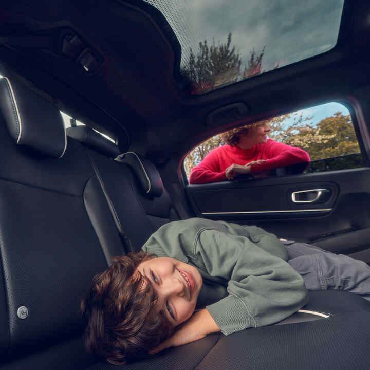 Egy gyermek fekszik a hátsó ülésen, az anya pedig a Honda e:Ny1 ablakában áll.