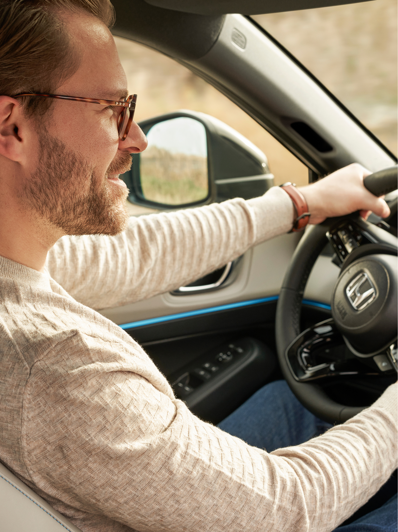 Egy szemüveges férfi egy Honda HR-V volánja mögött ül, az első utasülés felől nézve, mindkét kezét a kormányon tartja, és a műszerfal is látható.
