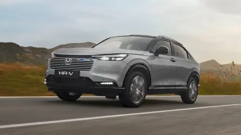 Egy modell sétál egy városi környezetben parkoló HR-V Hybrid előtt.