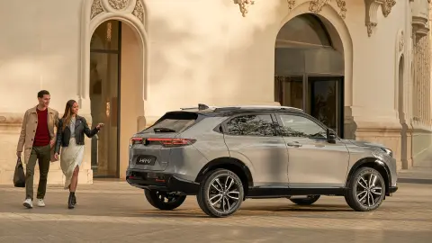 Oldalról készült felvétel a Honda HR-V modellről egy szálloda előtt, mellette sétáló párral. 