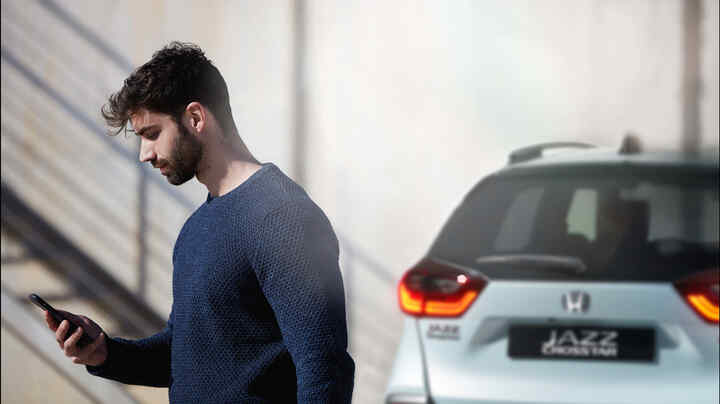 Egy személy egy okostelefont néz, a háttérben egy Honda Jazz Crosstar.
