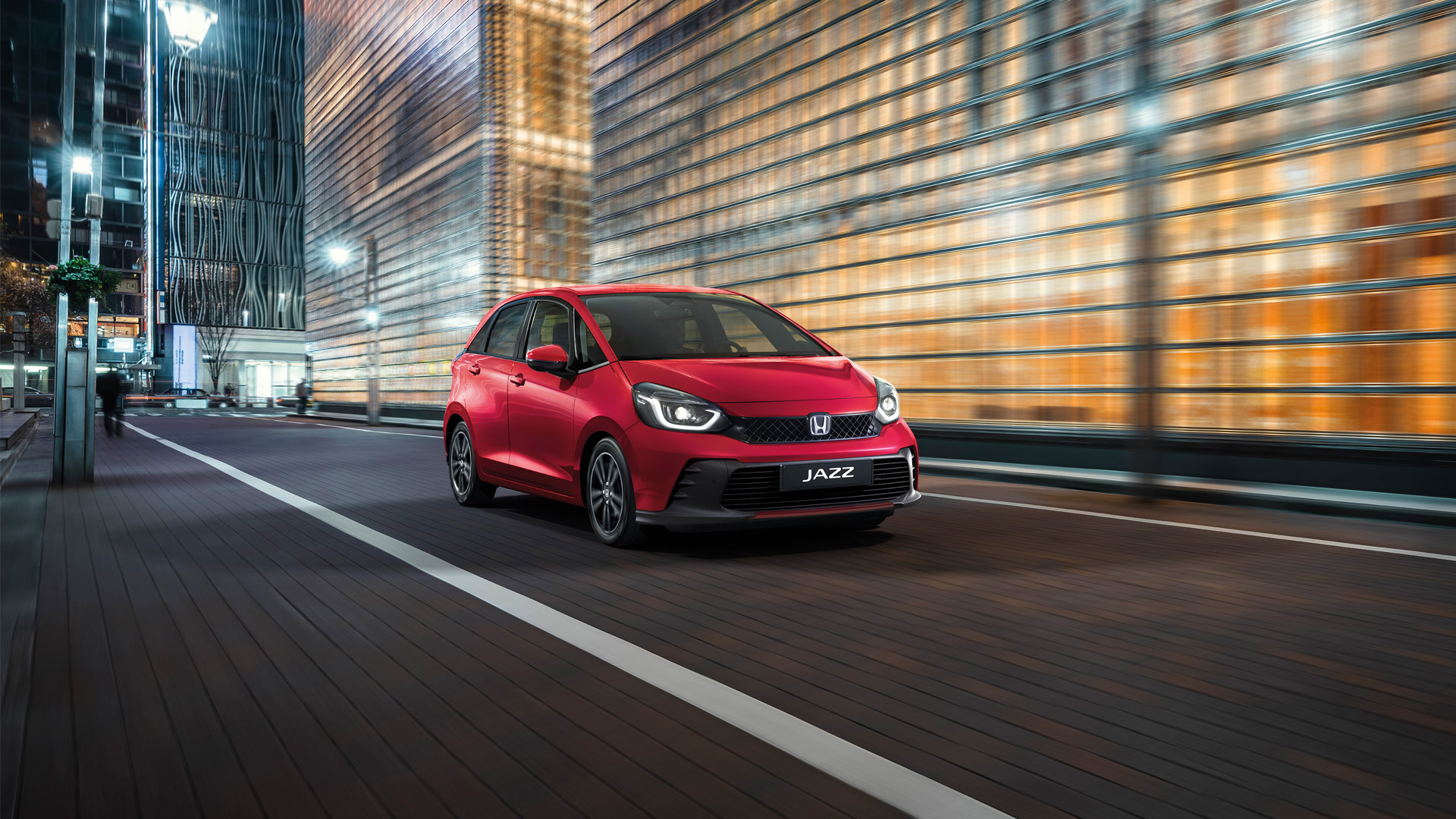 Elölről, háromnegyedes szögből készült felvétel a Honda Jazz modellről városi háttér előtt.