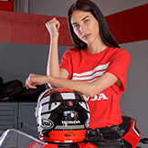 Egy piros Honda topot viselő hölgy, aki egy Honda motoros bukósisakra támaszkodik.