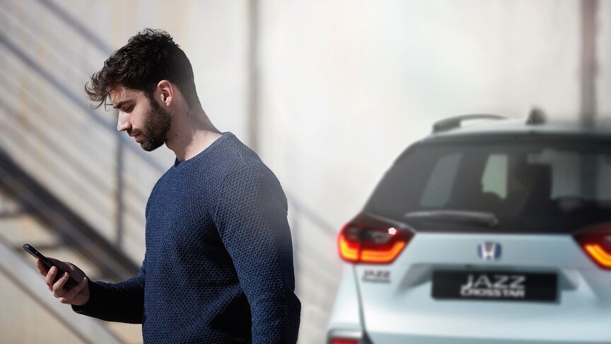 Egy fehér Honda e mellett álló hölgy, aki a My Honda Plus alkalmazást használja