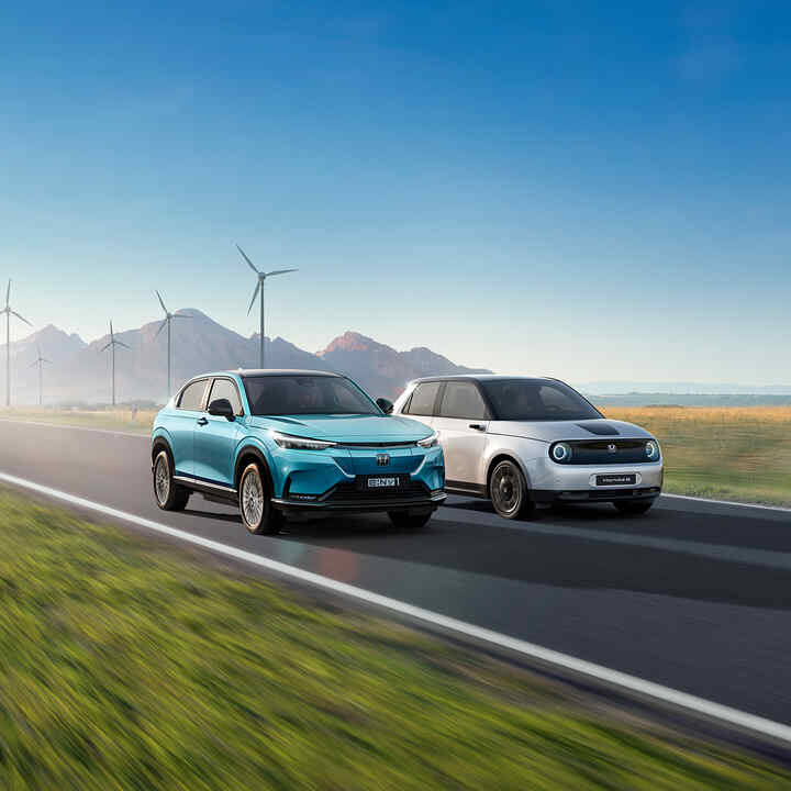 Egy Honda e:Ny1 és egy Honda e modell halad el egy szélerőműpark mellett.