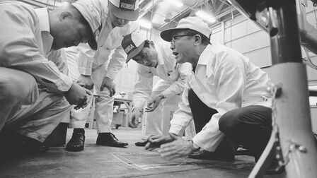 Soichiro Honda és a gyár alkalmazottjai fehér munkaruhában.