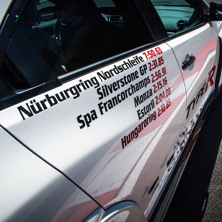 Közelkép a Honda Civic Type R-ről, a kép szélén köridők.
