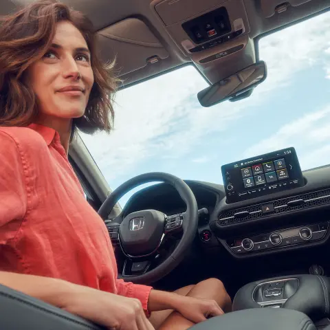 A Honda ZR-V hibrid vezetőülésében egy hölgy ül, aki az infotainment rendszer képernyőjét nézi.