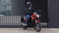Egy piros Honda CB125F elölről, háromnegyedes nézetben, egy motoros a leállított motorkerékpáron, városi környezetben