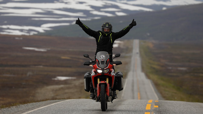 Magasba emelt karú férfi egy Honda Africa Twin motoron, Nordkapp útjain.