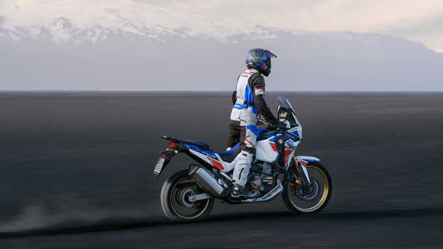 Hátsó háromnegyedes felvétel a Honda Africa Twin motorkerékpárról, amely homokdűnék között áll.