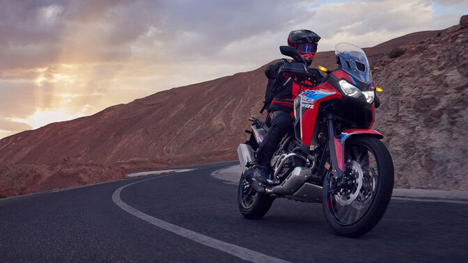 Fotómodell ül egy CRF1100L Africa Twin motorkerékpáron egy hegyvidéki úton.