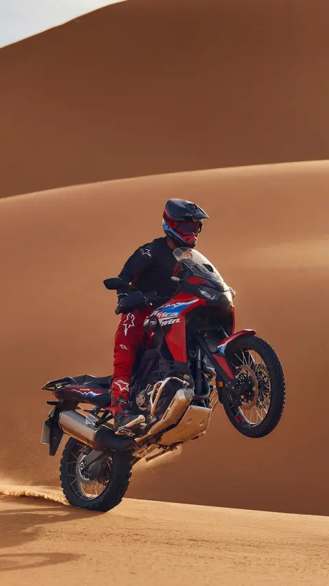 Fotómodell ül egy CRF1100L Africa Twin motorkerékpáron a sivatagban.
