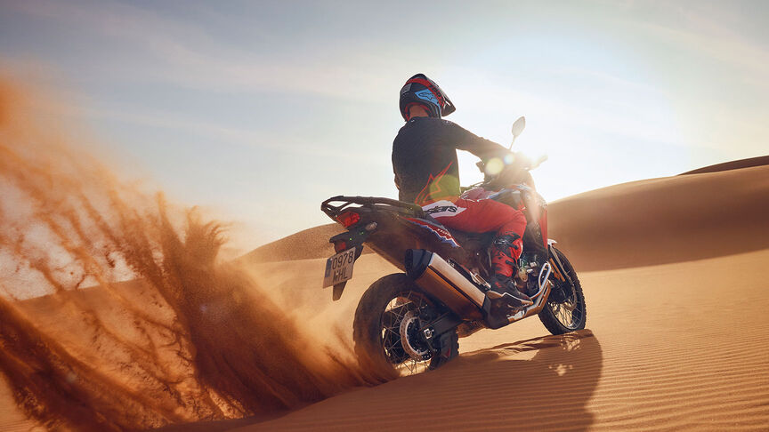 Fotómodell halad egy CRF1100L Africa Twin motorkerékpárral a sivatagban.