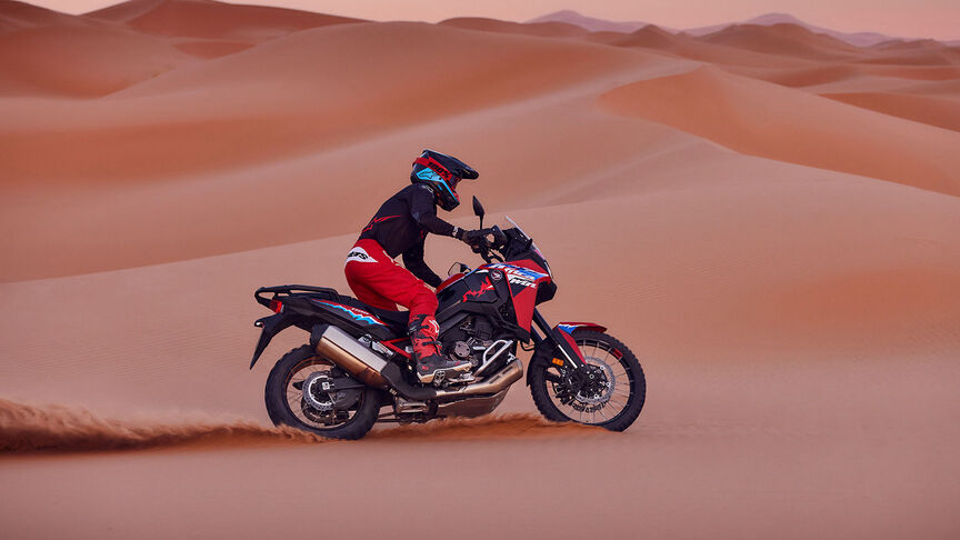 Fotómodell halad egy CRF1100L Africa Twin motorkerékpárral a sivatagban.