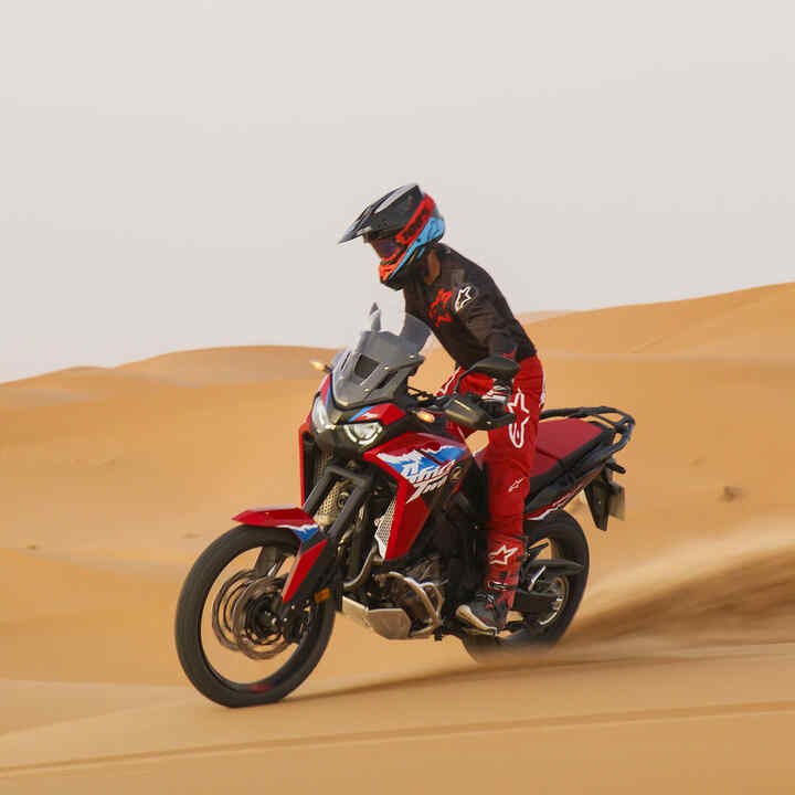 Fotómodell ül egy CRF1100L Africa Twin motorkerékpáron egy sivatagi úton.