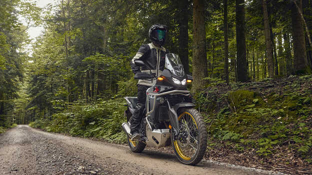 Modell egy Honda XL750 Transalp motorral erdei környezetben.