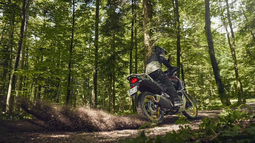 Modell vezet egy XL750 Transalp motorkerékpáron erdei környezetben.