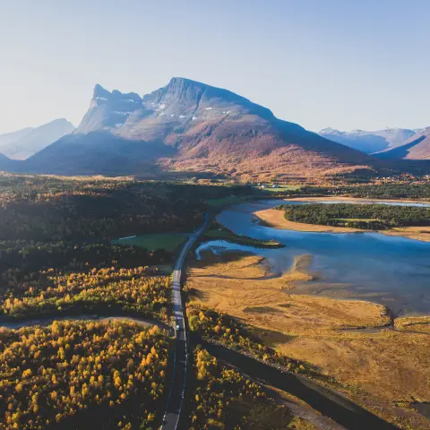 Klasszikus norvég nyári tájkép hegyek és fjordok között kanyargó úttal, kék égbolttal, Észak-Norvégia, Finnmark megye, drónfelvétel