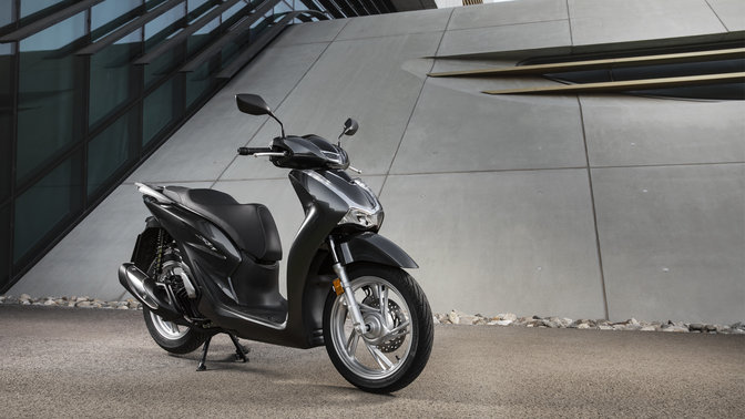 Honda Sh125i hátsó dobozzal és szélvédővel az utcán.