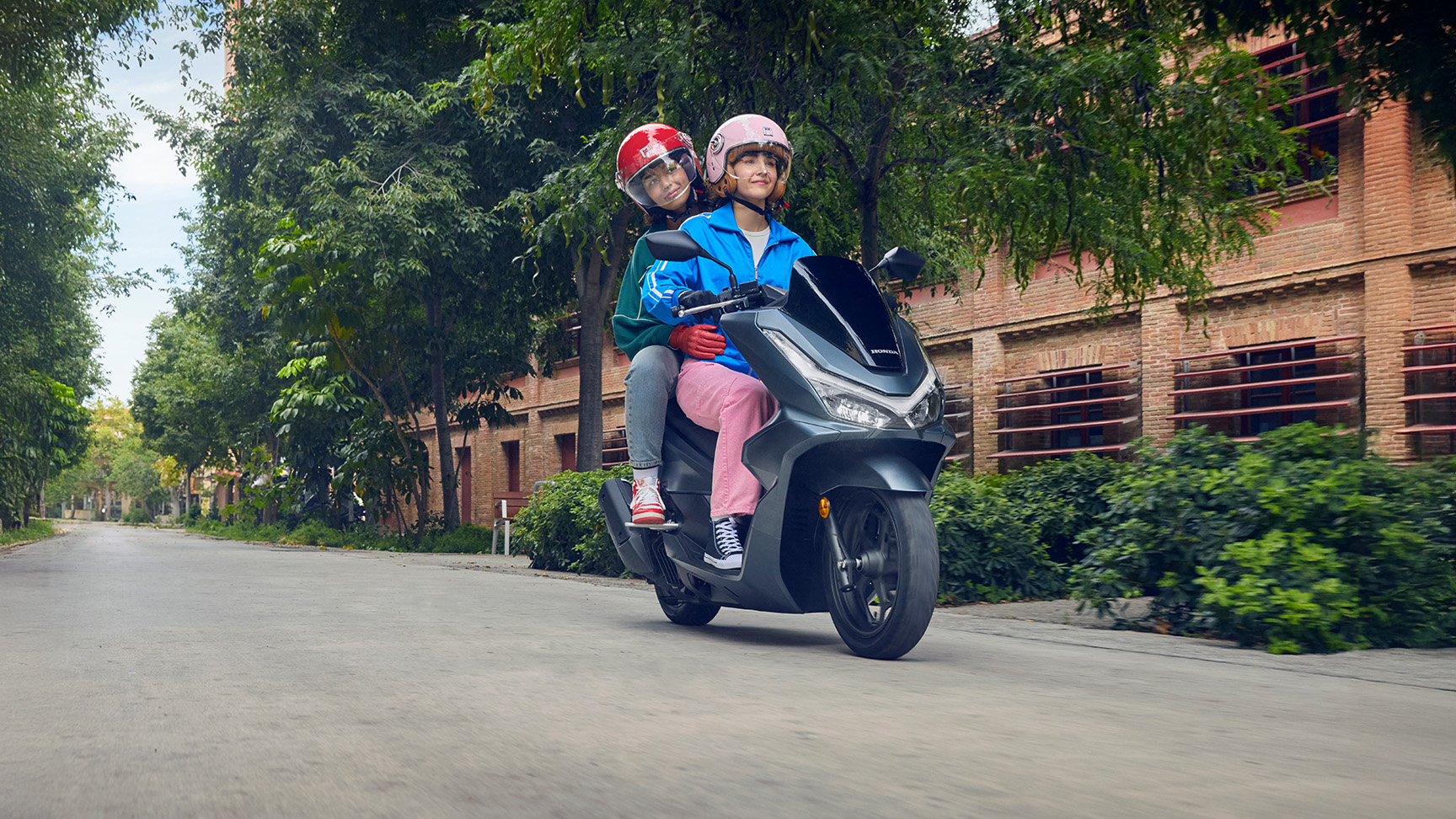 Modellek motoroznak a PCX125 motorkerékpáron városi környezetben.