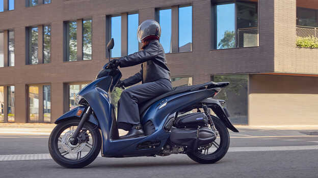 Oldalról készült felvétel a Honda SH350 modellről motorossal, városi környezetben.