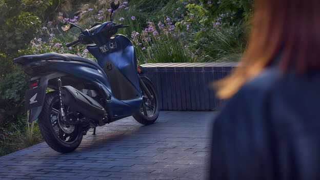 Hátulról készült felvétel a Honda SH350i modellről egy kertben. 