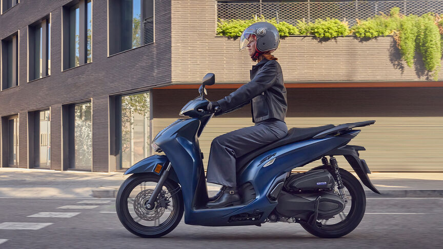 Oldalról készült felvétel a Honda SH350i modellről városi környezetben, női motorossal.