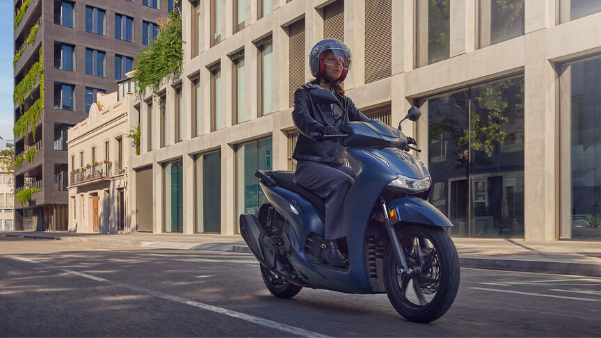 Oldalról készült felvétel a Honda SH350i modellről városi környezetben, női motorossal.