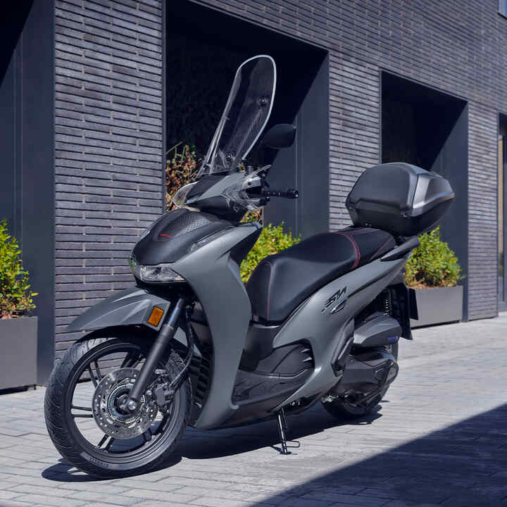 Elölről készült háromnegyedes felvétel egy álló Honda SH350i modellről egy épületben.