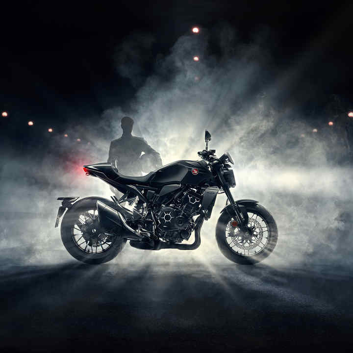 Honda CB1000R – Black Edition – jobb oldal, a motoros a motor mögött áll éjszaka, a ködben, fekete motor