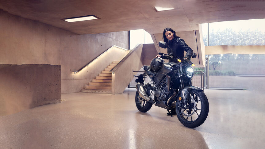 Honda CB300R háromnegyedes felvétel elölnézetből, és egy nő, aki a motort nézegeti egy stúdióban.