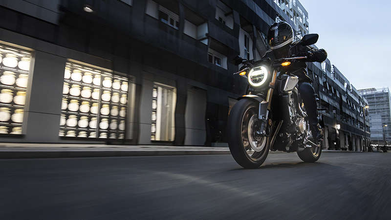 Háromnegyedes, elölről készült felvétel a CB650R Neo Sports Café bal oldaláról pilótával városi környezetben
