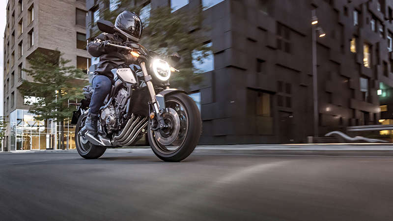 Háromnegyedes, elölről készült felvétel a CB650R Neo Sports Café jobb oldaláról pilótával városi környezetben