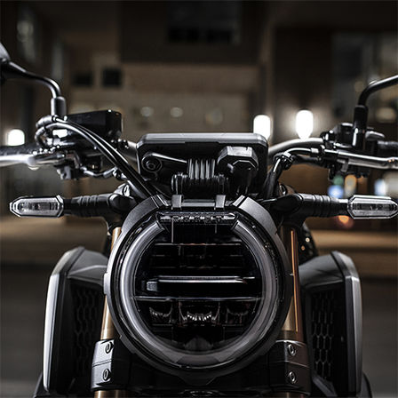 A CB650R Neo Sports Café elölről városi környezetben éjszaka, a fényszóróra fókuszálva 
