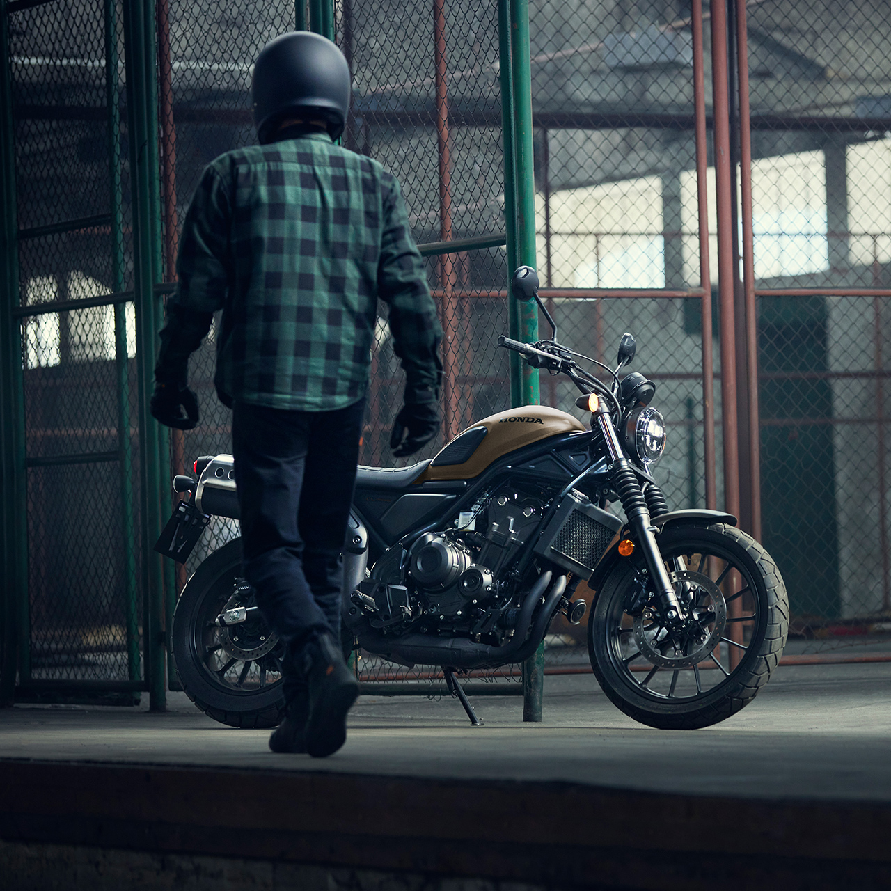 Motoros sétál egy parkoló Honda CL500 motorkerékpár mellett egy raktárban.