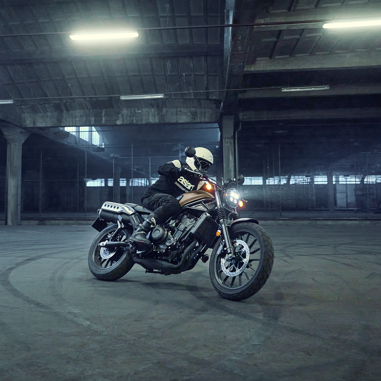 Fotómodell a Honda CL500 motorkerékpár nyergében egy parkolóban.