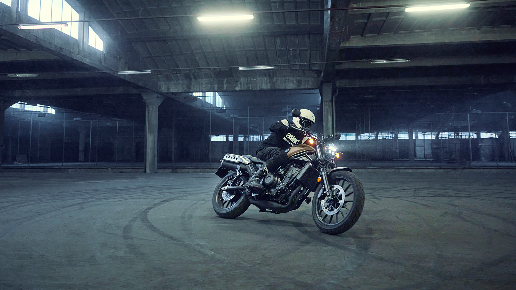 Fotómodell a Honda CL500 motorkerékpár nyergében egy parkolóban.